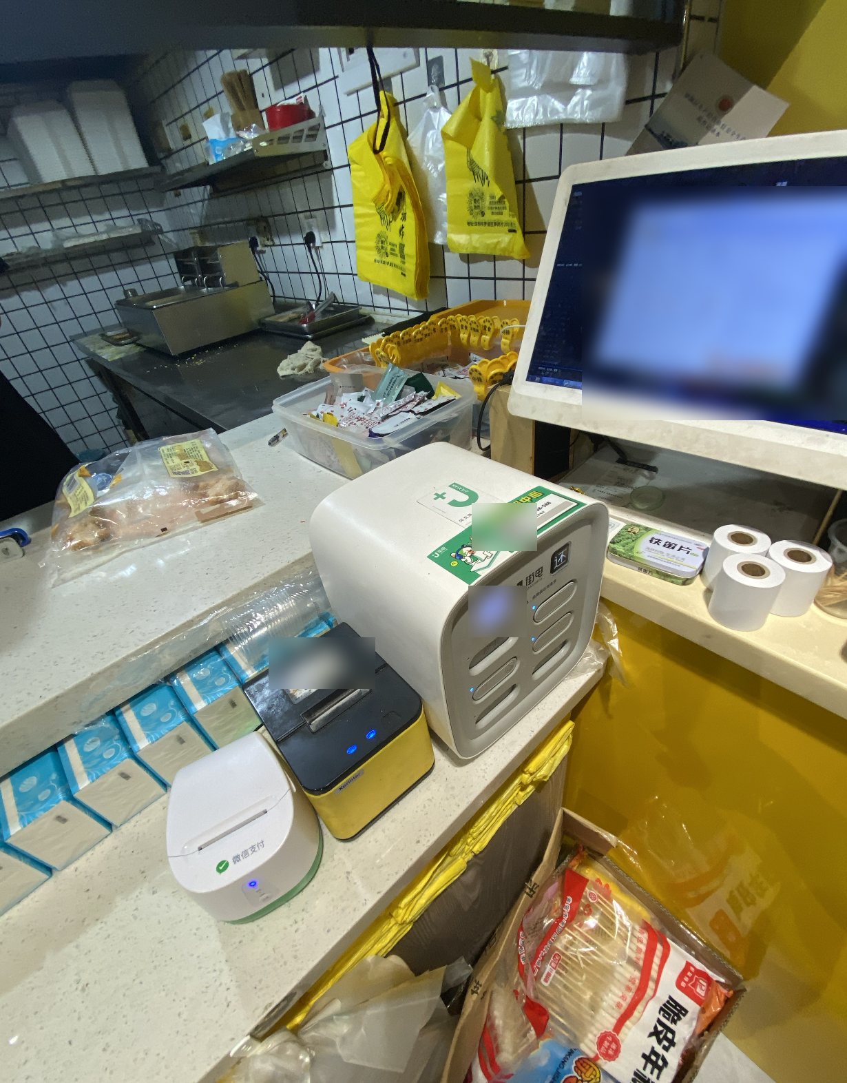 A shop counter with two receipt printers, a power-bank kiosk, and a POS screen