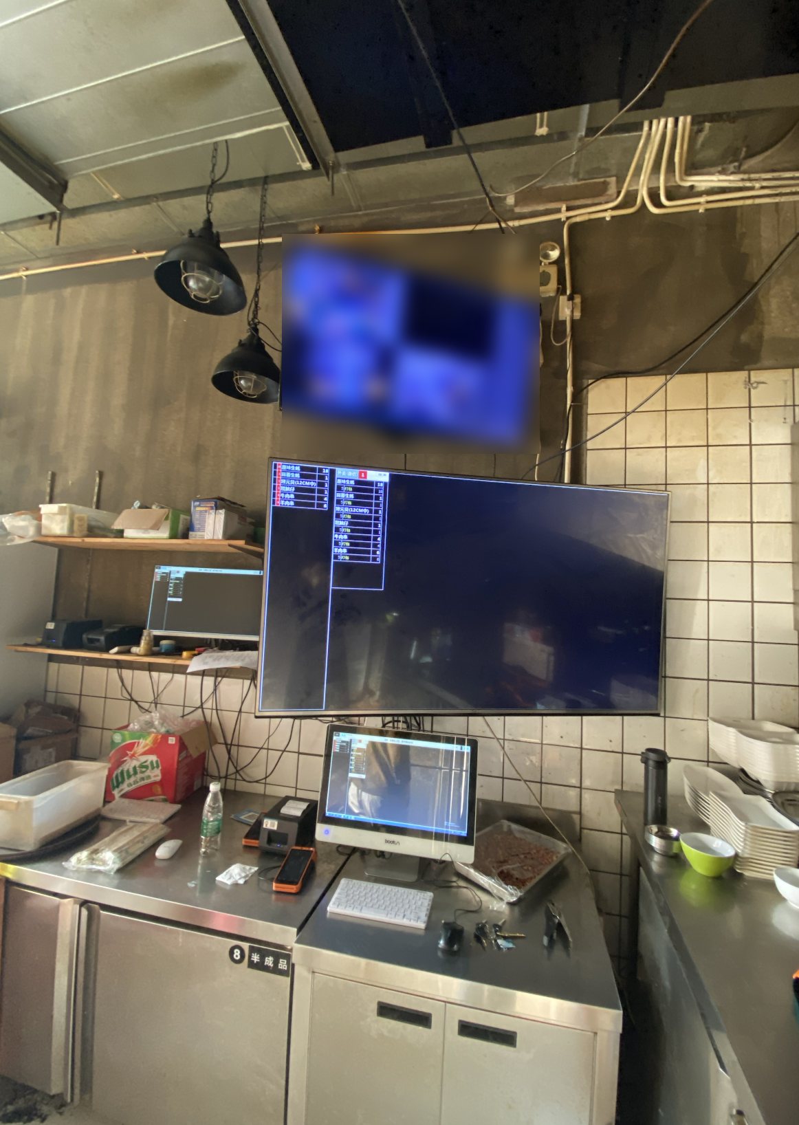 A restaurant kitchen with an order display screen on the wall and a CCTV monitor above it