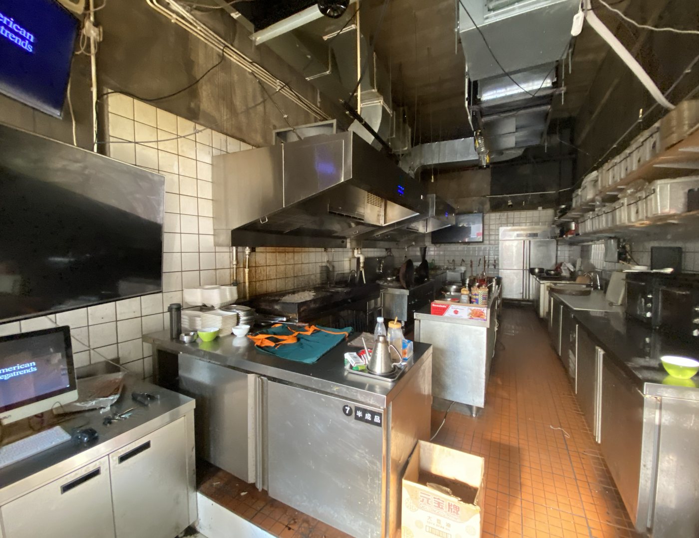 A narrow commercial kitchen with stoves, hoods, and prep stations
