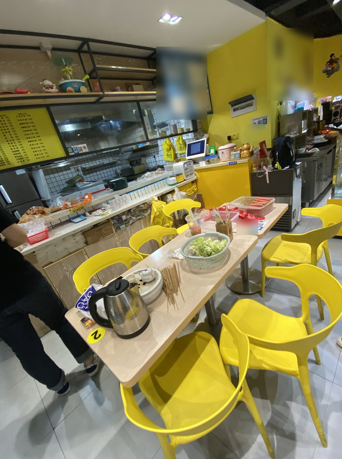 A small counter-service shop with yellow chairs, a few tables, and a kitchen window
